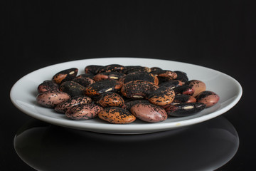 Lot of whole stained purple bean on white ceramic plate isolated on black glass