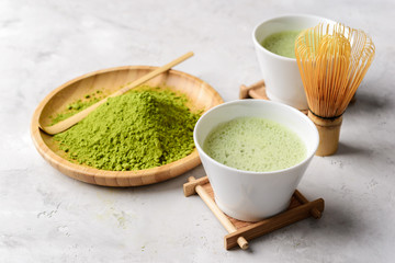 Matcha green tea in two white Tawan, tasaku and a bamboo whisk on white concrete background