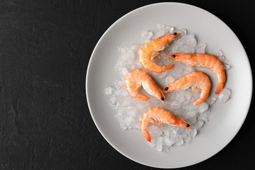 Boiled shrimp lying in the ice on a light round plate on  black  background