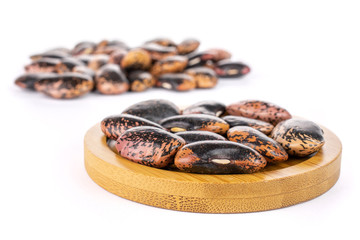 Lot of whole stained purple bean on round bamboo coaster isolated on white background