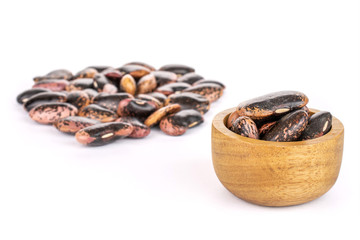 Lot of whole stained purple bean part is in the back and part is in the front in tiny wooden bowl isolated on white background