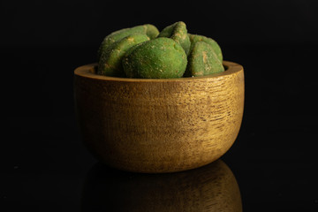 Lot of whole spicy green wasabi peanut in tiny wooden bowl isolated on black glass