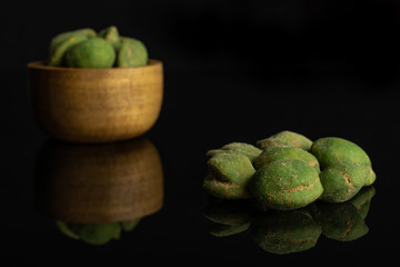 Lot of whole spicy green wasabi peanut small group is in the front and the rest is in tiny wooden bowl isolated on black glass