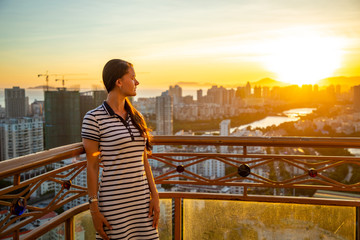 Young woman looks at view of Sanya city with river at sunset light, Hainan province, China