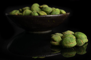 Lot of whole spicy green wasabi peanut small group is in the front and the rest is in dark ceramic bowl isolated on black glass