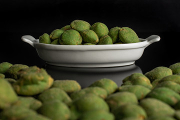 Lot of whole spicy green wasabi peanut in white oval ceramic bowl isolated on black glass
