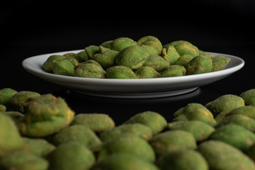 Lot of whole spicy green wasabi peanut on white ceramic plate isolated on black glass