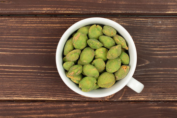 Lot of whole spicy green wasabi peanut in white ceramic cup flatlay on brown wood