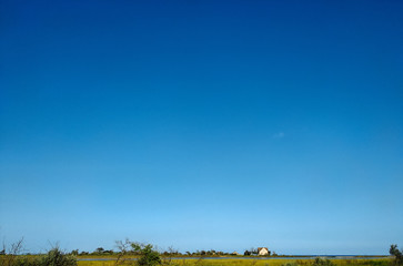 Summer landscape with a green field and blue sky and a small house on the horizon. The concept of harmony with nature, the life of the farmer. Copy space.
