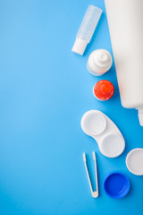 Optical corrective medical soft contact lenses for eyes in white plastic case with storage solution, accessories and care products in plastic bottles on blue background, Cleaning