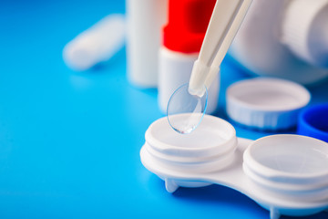Optical corrective medical soft contact lenses for eyes in white plastic case with storage solution, accessories and care products in plastic bottles on blue background, Cleaning