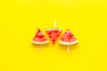 Cut watermelon on stick for break with fruit popsicle on yellow background top view