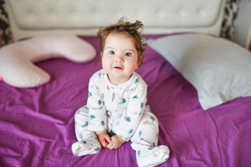Fototapeta premium the baby is sitting on the bed. Cute girl on the bed in the bedroom