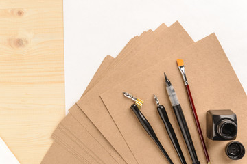 Calligraphy concept, accessories and tools for handwriting,ink, brush,writing training,blank sheets of white paper and cardboard crafting on wooden table,place for text