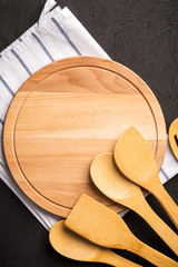 Wooden kitchen utensils and empty round tray for cooking on dark background,