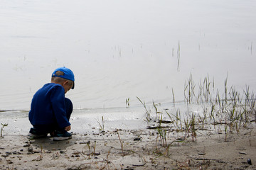 little boy sits alone on the shore near the water