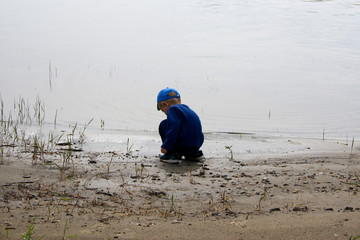 little boy sits alone on the shore near the water