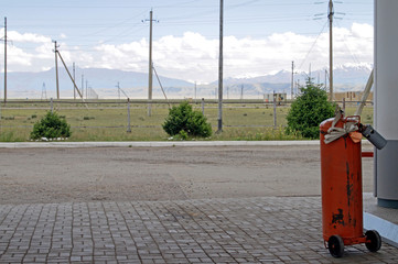 Red tank at a gas station in Kyrgyzstan, with power lines and the mountains in the background