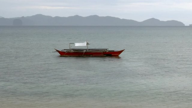 Traditional small boat laying still in the sea, island in the background on a cloudy day.