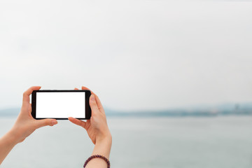 Mock up. Women's hands holding the phone horizontally. In the background sea and sky. Copy space. Isolate
