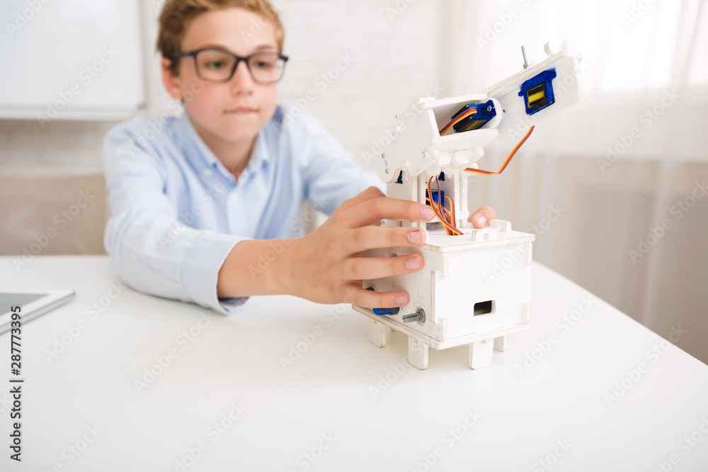 Poster Smart schoolboy constructing electronic robot in class