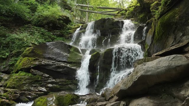 Wonderful mountain waterfall cascade falls near large grey rocks with green moss and green leaves. Carpatian waterfall Shypit, Pylypets, Ukraine