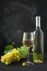 Bottle of white wine with wineglass, ripe grape on black wooden table.