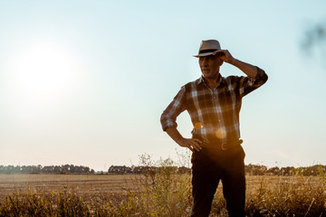 senior man touching straw hat in wheat field
