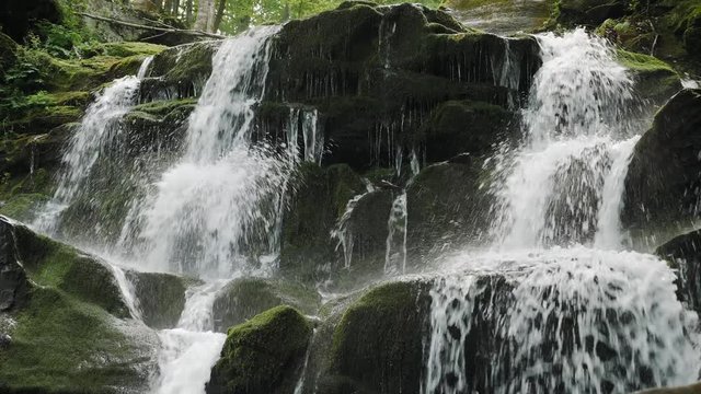 Shypit waterfall on the Pylypets River. Beautiful mountain waterfall cascade falls near large grey rocks with green moss and green leaves. 4k video