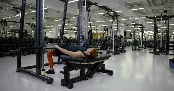 Athletic girl in the gym doing lying exercises on her legs with a barbell, raises and lowers the pelvis and shakes her buttocks.