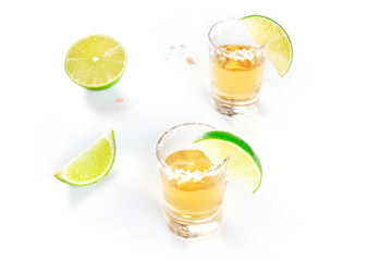 Golden tequila shots with lime slices and salty rims on white with copyspace
