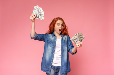 Excited Redhead Girl Holding Plenty Of Money On Pink Background