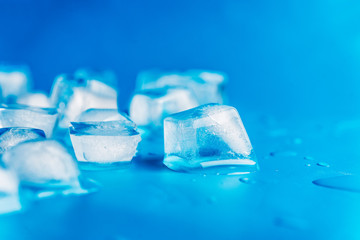 Ice cubes and water drops scattered on blue background