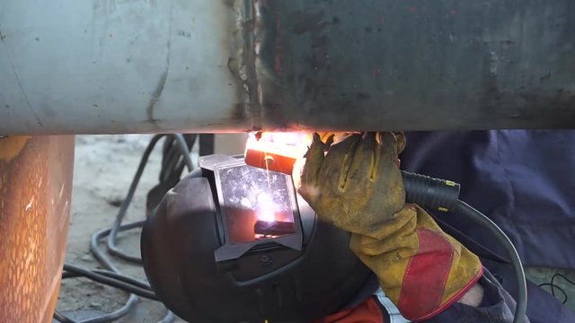A welder welds technological pipelines with manual arc welding for an oil refinery in Russia. Welded joint.