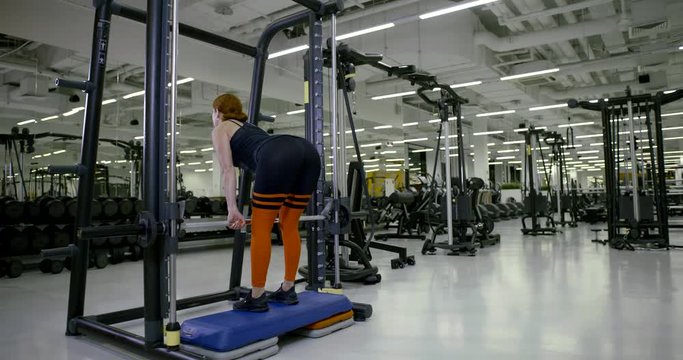 Athletic girl in the gym doing deadlift with a barbell, a view from the back.