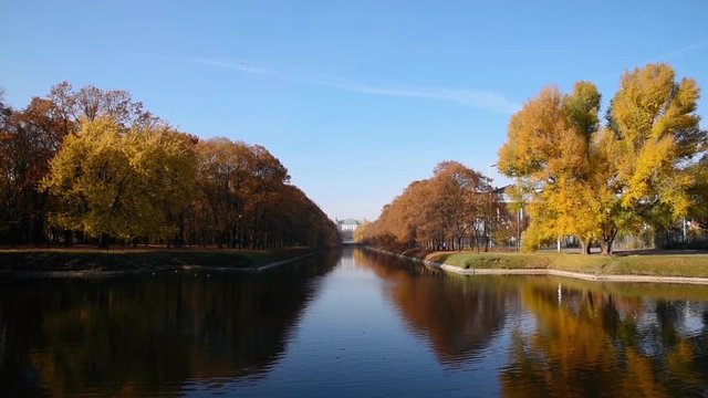 City park Royal Lazienki with pond or lake and  Ujazdowski Castle on background with blue sky, trees and fallen leaves at autumn. Warsaw, Poland, Europe. Panoramic view