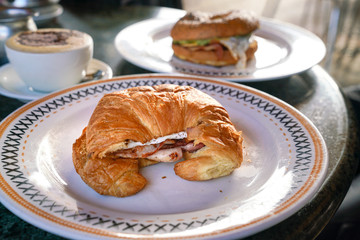 Croissant with bacon and eggs and bagel with coffee at the background