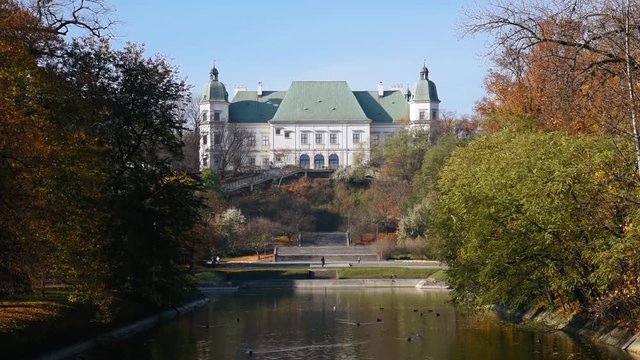 City park Royal Lazienki with pond or lake and  Ujazdowski Castle on background with blue sky, trees and fallen leaves at autumn. Warsaw, Poland, Europe. Close-up view