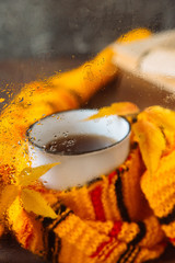 a mug of hot tea wrapped in a bright scarf behind the glass with raindrops