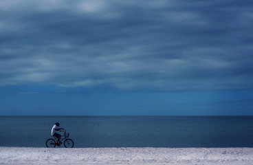 Naklejka premium A cyclist rides on the surf line along the beach. The coast of the ocean, the minimalism of the lines. Florida. USA.