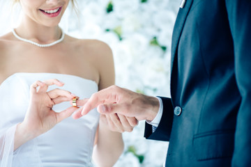cropped view of smiling bride putting wedding ring on finger