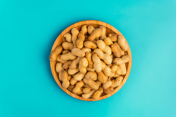 Inshell peanuts in a wooden plate on a blue background, space for text