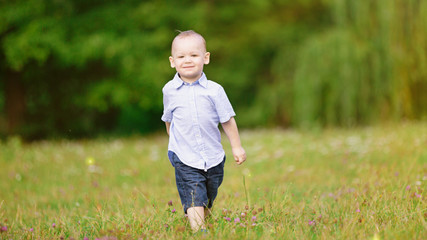 Little boy marching on the green grass in the park