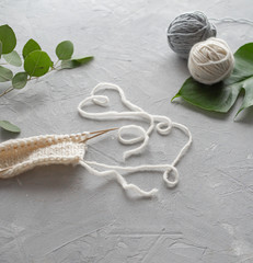 On a gray background, eucalyptus leaves and monstera, a heart of thread, two balls of wool and a knitting scarf with wooden spokes. The concept of needlework, handmade.
