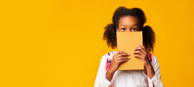 African American Schoolgirl Covering Face With Book, Yellow Background