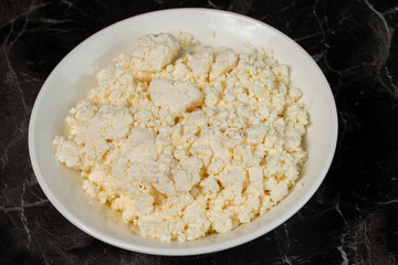 White plate with cottage cheese on a black background