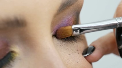 Fashionable multi-colored eye shadow chameleon with yellow purple gray silver color on the eyelid of a beautiful girl model with brown eyes. Professional cosmetic makeup. Eye close up view