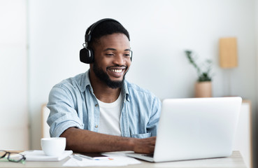 Smiling freelancer working on laptop and listening music in headphones