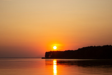 The  horizontal photo of golden sunset above the river or sea. Reflection in the water like fire. Seacoast.