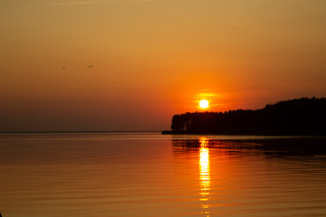 The  horizontal photo of golden sunset above the river or sea. Reflection in the water like fire. Seacoast.